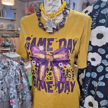 A yellow shirt with a purple bow that says game day on it.